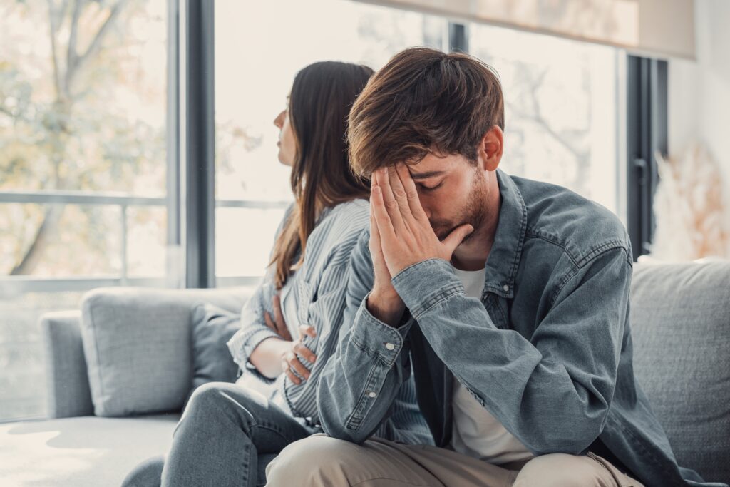 woman sitting on the couch talking to man with his hands over his face, mental health issue