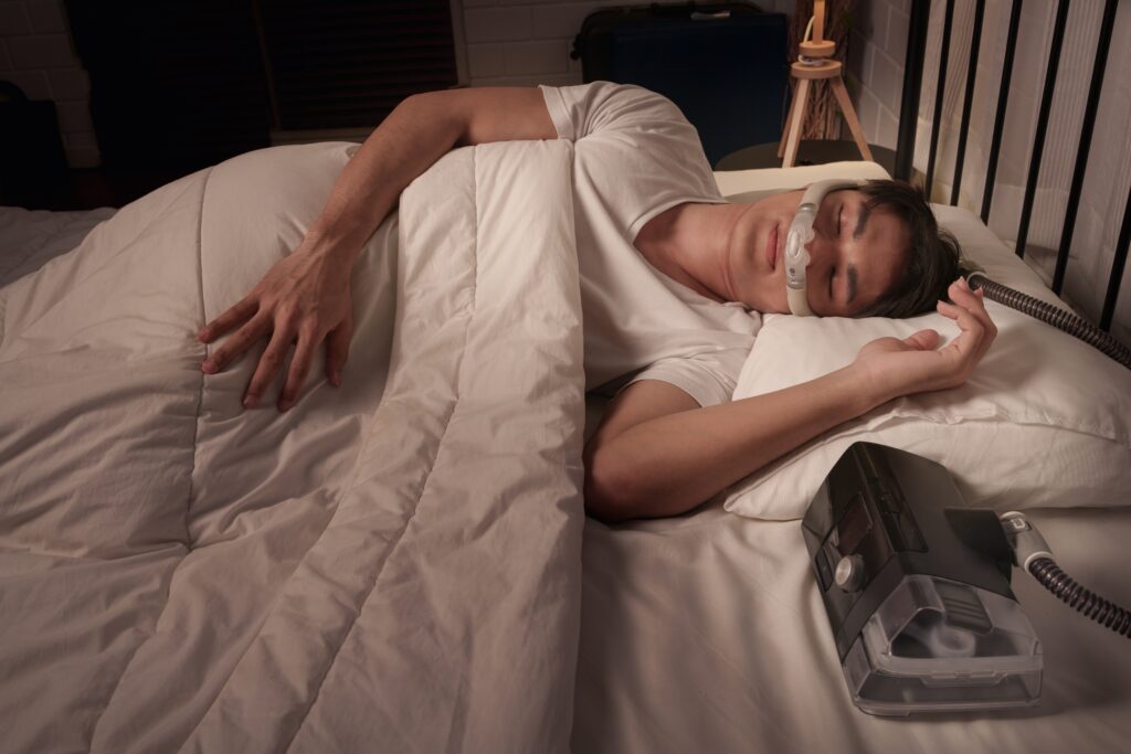 Peaceful Asian male asleep using CPAP mask and machine for obstructive sleep apnea and snoring
