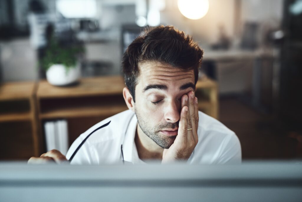 fatigued man rubbing his eyes at his desk
