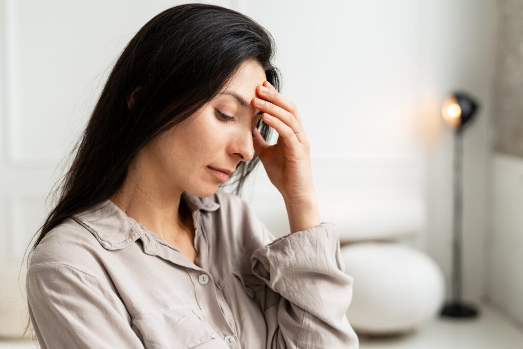 Woman feeling tired and unwell, holding hand to her forehead, experiencing fatigue