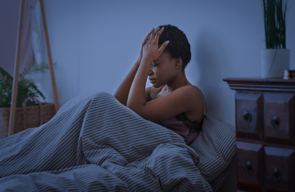 woman sitting up in bed holding head and having trouble sleeping