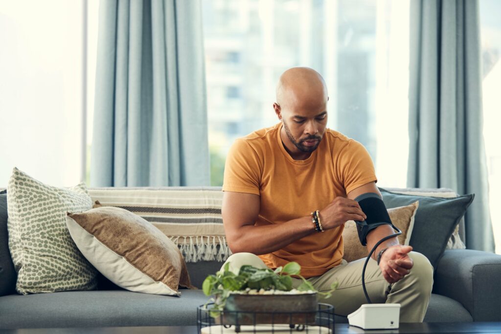 A young man having his blood pressure taken as he sits on his couch at home.